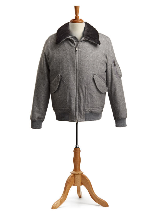 The ISAIA® Aviator Jacket displayed on a wooden mannequin stand. The jacket has a zippered front, is made from a light gray Cashmere Silk blend, and features a luxurious dark brown faux fur collar. Two large pockets with triangular flaps are seen on both sides of the lower front section and a smaller zippered pocket is located on the upper right sleeve. The cuffs and hem of the jacket are made from a ribbed knit material in a matching grey color.